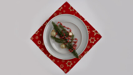 Festive table setting featuring white plates arranged on a red star-patterned tablecloth, adorned with evergreen sprigs and decorative ornaments for a joyful holiday atmosphere