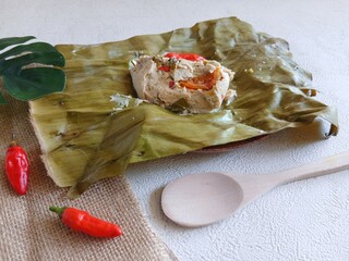 botok tofu wrapped in banana leaves on a white plate and white background