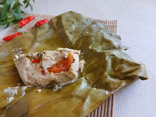 botok tofu wrapped in banana leaves on a white plate and white background