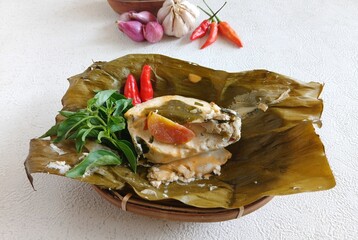 botok tofu wrapped in banana leaves on a white plate and white background