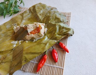botok tofu wrapped in banana leaves on a white plate and white background