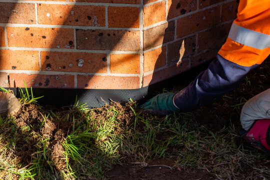 Handyman putting water protective dampcourse tape against brick base of house