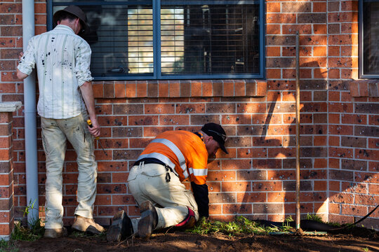 Handyman putting water protective dampcourse against brick base of house