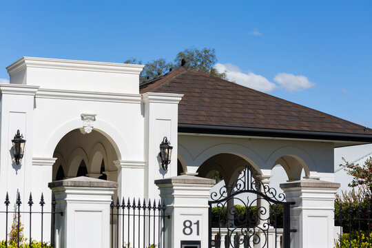 sunlit house exterior behind fence and gate with wrought iron