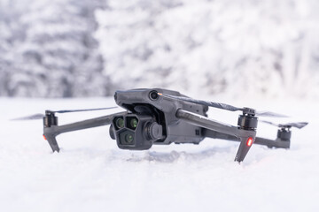 A black drone on the background of a winter forest. Winter aerial photography and aerial photography from drones while traveling. Features of quadcopter operation in the cold season. A black drone on