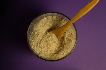 Inactive nutritional yeast flakes supplement in wooden spoon and glass jar top view. Cheese substitute for vegan cooking