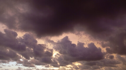 Dramatic dark storm clouds gather over a tranquil beach at dusk, reflecting soft golden light onto the crashing ocean waves