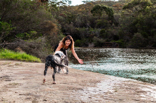 A joyful woman with her dog near a peaceful riverbank surrounded by trees