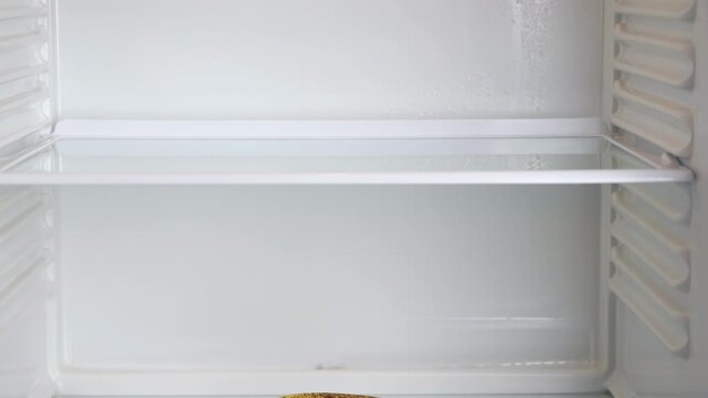 A lonely banana in an empty refrigerator. A lonely banana lies on a glass shelf inside an empty refrigerator. Empty shelves in refrigerator. Weight loss diet concept