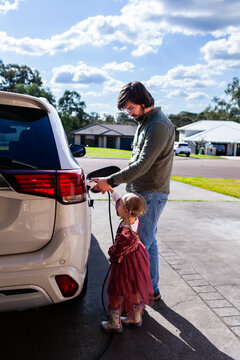 Dad with young daughter unplugging hybrid ev vehicle together in suburban driveway