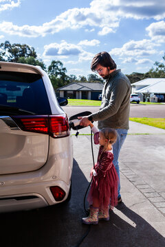 Dad with young daughter unplugging hybrid ev vehicle together in suburban driveway