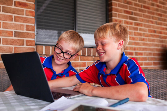 Two young boys doing schoolwork on laptop in backyard outside home       