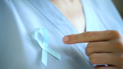 A female doctor in medical uniform pins a blue satin ribbon. November is Prostate Cancer Awareness Month, highlighting diagnosis and timely treatment.