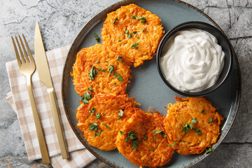 Vegetarian fritters from sweet potato served with sour cream closeup on the plate on the table. Horizontal top view from above
