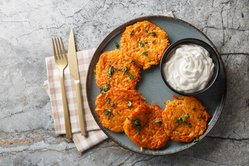 Sweet Potato Hash Browns with crispy edges and a buttery center served with sour cream closeup on the plate on the table. Horizontal top view from above
