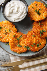 Pan-Fried Sweet Potato Fritters served with sour cream closeup on the plate on the table. Vertical top view from above