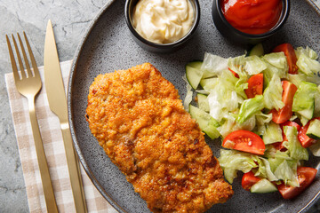 Breaded Sicilian Steak or Bistecca Alla Siciliana with salad and sauces closeup on the plate on the table. Horizontal top view from above