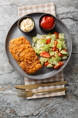 Sicilian breaded beef steak served with fresh salad and two sauces close-up on a plate on the table. Vertical top view from above