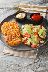 Sicilian breaded beef steak served with fresh salad and two sauces close-up on a plate. On the table. Vertical