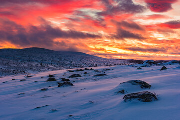 Winter sunrise in Sweden showcases vibrant colors over snow-covered hills and rocks