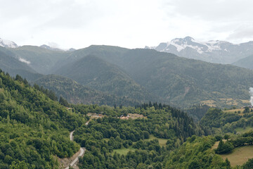 Naklejka premium Scenic landscape with rolling hills and a winding trail through lush greenery, leading to distant mountains under a cloudy sky