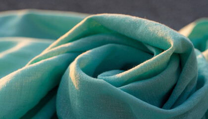 A close-up shot of a soft, flowing turquoise fabric with gentle folds and highlights.