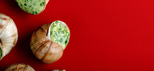 Close-up of escargot stuffed with garlic herb butter on a vibrant red background, creating an appetizing gourmet food presentation. © alesmunt