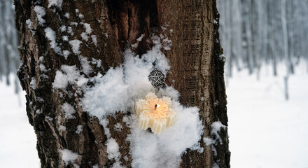 snowflake shape candle, pentacle amulet on snowy tree trunk, winter forest background. fairy tale...