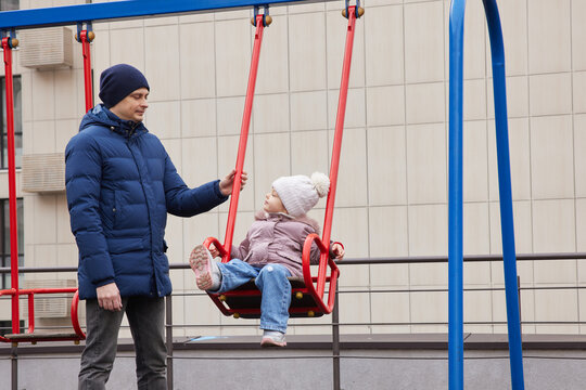 Father and daughter enjoying time together on a playground swing during winter - Powered by Adobe