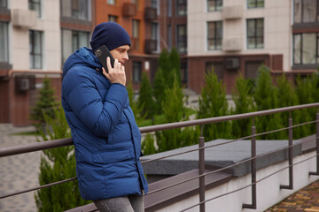 Man talking on mobile phone while leaning on railing in urban setting
