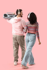 Young couple in headphones with boombox on pink background, back view
