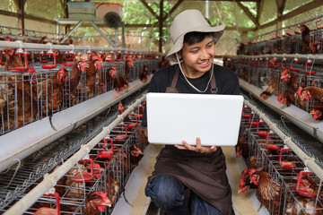 Happy Young Farmer Uses Laptop in Chicken Coop to Manage Farm Operations © Gatot