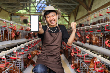 Happy Young Farmer in Chicken Coop Shows Phone With Blank Screen for App Promotion © Gatot
