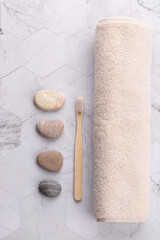 Top view vertical of rolled beige towel with wooden brush and natural stones on light geometric stone background. Minimalist spa style with copy space. Concept of self care and relaxation