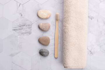 Top view horizontal of beige towel with wooden brush and decorative stones on light geometric stone surface. Natural and relaxing style with copy space. Concept of wellness routine and spa lifestyle
