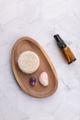 Top view vertical of solid shampoo bar on wooden tray with amber cosmetic bottle and decorative stones over light stone background. Minimalist style. Concept of organic hair care and wellness