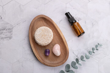 Top view horizontal of solid shampoo bar on wooden tray with amber cosmetic bottle, decorative stones and eucalyptus branch over light stone background. Copy space. Concept of natural self care 