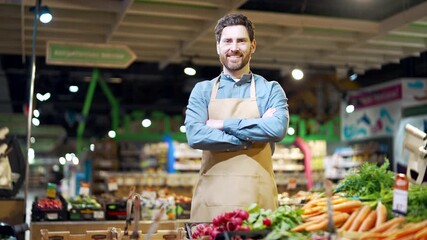 Portrait male salesman in apron looking at camera near a counter with vegetables in market or grocery store. A male greengrocer or small business owner smiling in supermarket Professional Staff