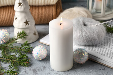 Burning candle with Christmas balls and book on grunge table, closeup