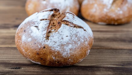 Warm, freshly baked artisanal bread rolls with flour dusting presented on a rustic wooden table in a cozy indoor setting, close-up food photography.