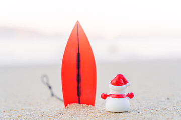 Sandy Christmas Snowman is watching the waves, standing on beautiful beach with a surf board - horizontal version in Patong Beach, Phuket, Thailand