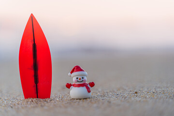 Sandy Christmas Snowman is watching the waves, standing on beautiful beach with a surf board - horizontal version in Patong Beach, Phuket, Thailand