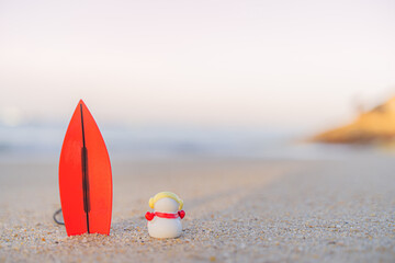 Sandy Christmas Snowman is watching the waves, standing on beautiful beach with a surf board - horizontal version in Patong Beach, Phuket, Thailand