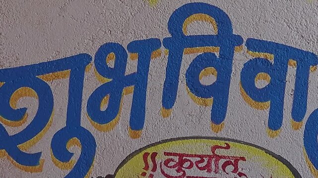 Traditional Indian wall art uses the Devanagari script to announce a wedding. The blue text says "Shubh Vivah" (Auspicious Marriage), and red text offers a blessing: "May there always be auspicious.