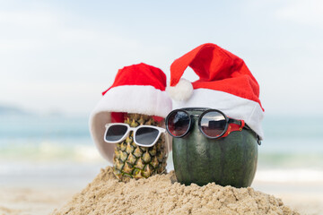 Santa Claus pineapple and watermelon couple wearing stylish sunglasses on the sand contrasting with the sea. wearing a christmas hat Christmas and New Year holiday ideas on the beach, Patong, Phuket
