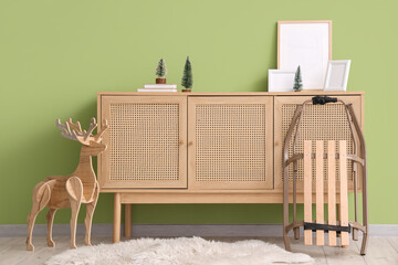 Chest of drawers with frames, Christmas decor and sled near green wall in room