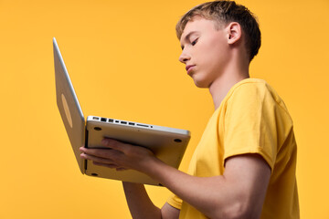 Young man in a yellow shirt uses a laptop against a bright yellow backdrop, illustrating focus, learning, and digital work with technology and portable device