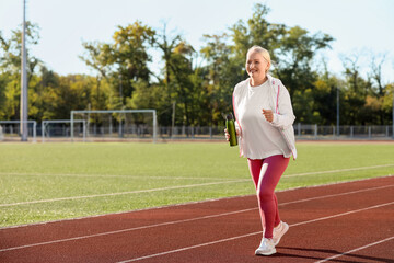 Sporty senior woman with water bottle running at stadium