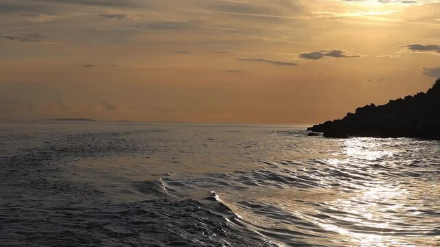 Beautiful sunset seascape with waves rolling against a dark rocky shore