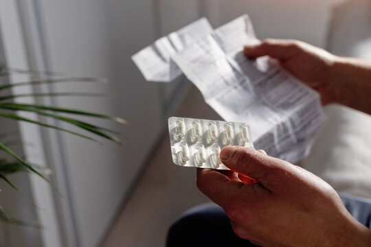 Closeup of male hands holding pills package and reading medication instruction information about dosage and side effects, painkiller.